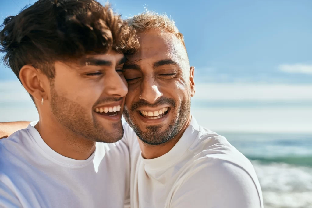 Same sex couple at the beach smiling while embracing