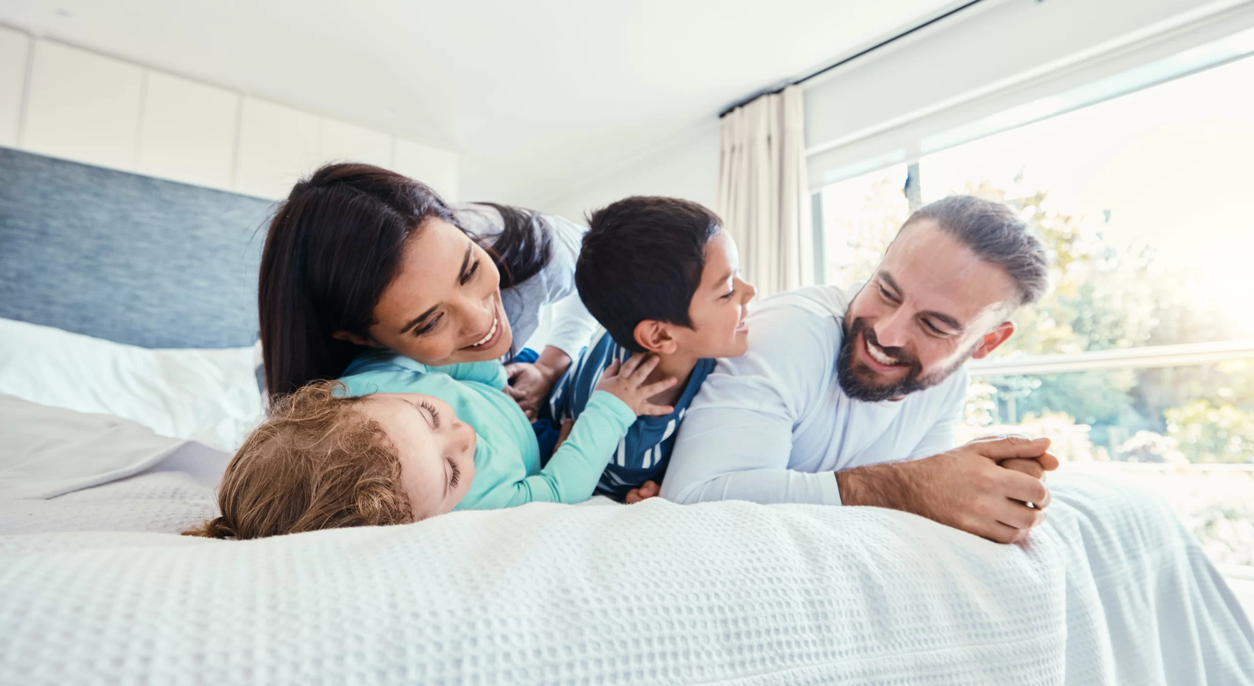 Family with two kids on the bed at home smiling and laughing together