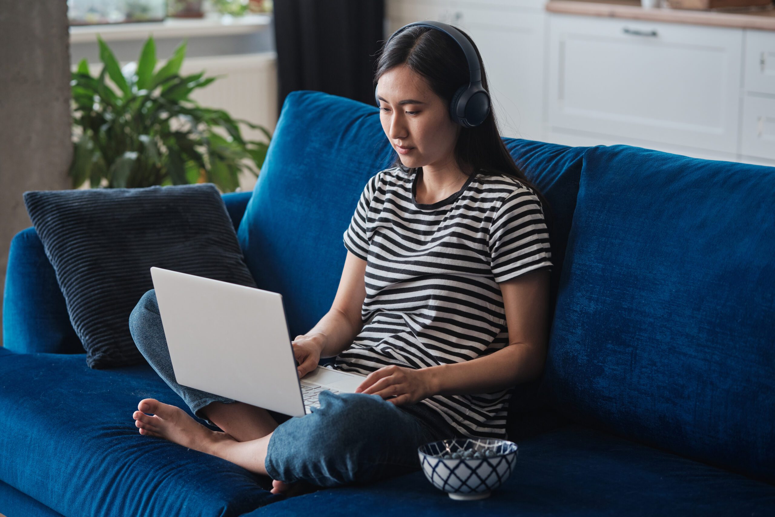 A focused woman wearing headphones sitting on sofa using laptop